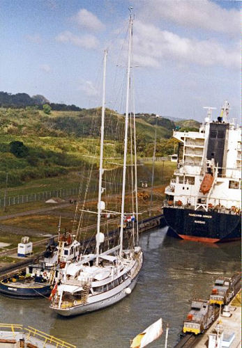 image of the Panama Canal, within the locks. There is one large ship in the background; there is a smaller boat and a tug in the foreground. 