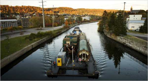 Image of a tugboat pulling a barge with large equipment on it.