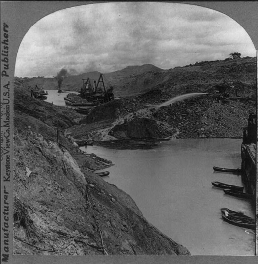 Image of the Panama Canal will a mound of dirt that has blocked the passage way. There are various boats that are blocked on either side of the landslide.