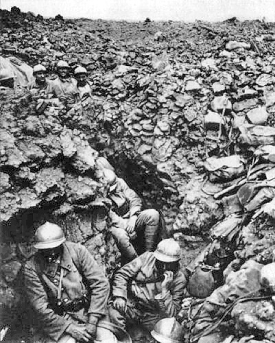 Image of soldiers in a trench with gas masks. The trenches are very muddy. There are some soldiers in the background standing in the trenches.