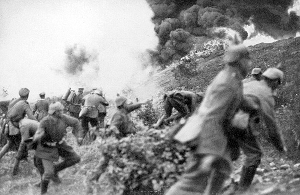 Image of soldiers using flamethrowers and hand grenades to aim at the top of a hill where there are huge flames and large billows of smoke.