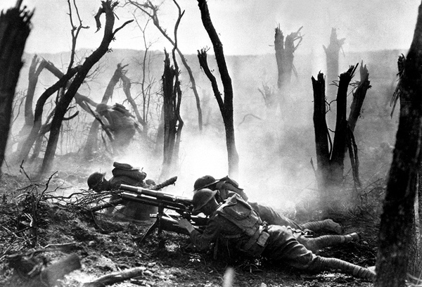 Image of three soldiers lying on the ground behind their guns. The trees of the forest are bare and there is dense fog surrounding them.