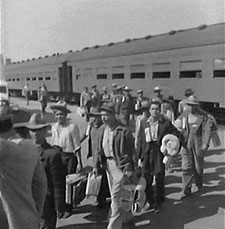 Several men walking off a train, carrying luggage