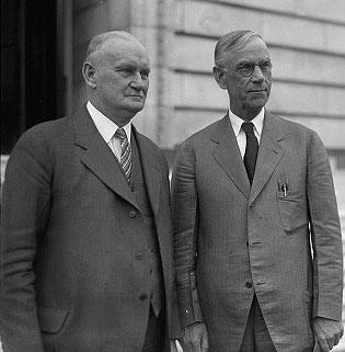 A photograph of US Representatives Hawley and Smoot in 1929 standing side by side. They are both men in late middle age wearing suits and ties