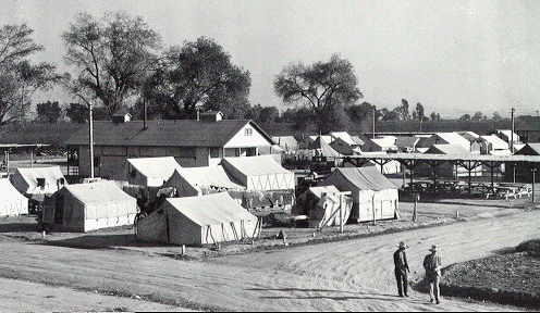 Photo of a weedpatch camp, with more than twenty visible tents and one wooden building.