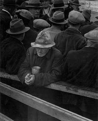 Image of several men lined in several rows. All are dressed in coats and hats. All men are facing away from the camera except for one man in a tattered hat; he has a tin cup.