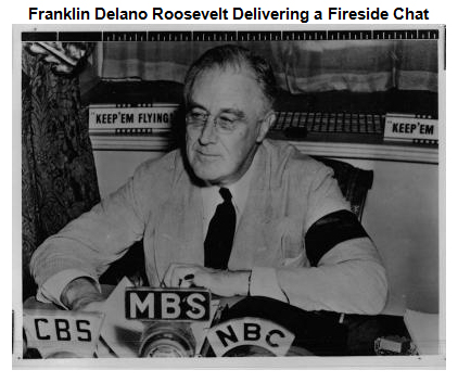 Photo of FDR sitting at a desk behind a bank of microphones