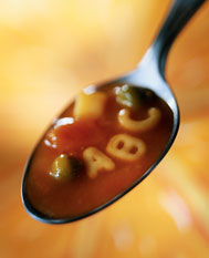 A spoon with some soup on it, a red broth, a couple vegetables and 'A, B,C' noodles