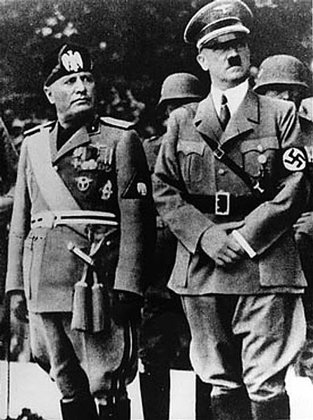 Image of Benito Mussolini, standing on the left wearing his military uniform and hat. Adolf Hitler standing in the right, wearing his military uniform and hat.