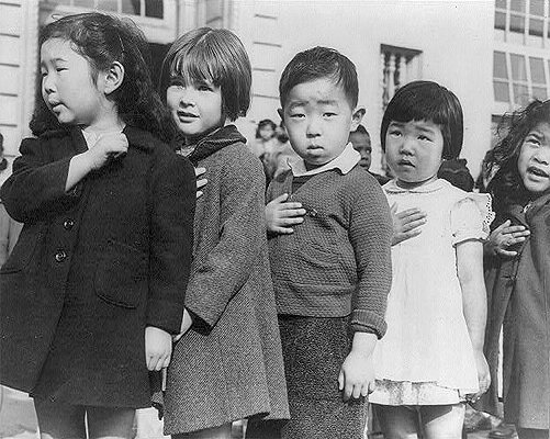 Japanese American children in an internment camp saying the Pledge of Allegiance. The children are all under five years old and holding their hands over their hearts.