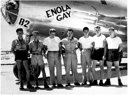 The crew of the bomber 'Enola Gay' standing on the runway near the nose of their bomber. They are 7 men in their 20s or 30s wearing casual military clothing.