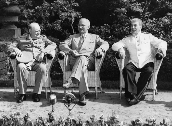 A photo of Winston Churchill, Harry Truman and Joseph Stalin sitting next to each other outdoors on a bench in Potsdam, Germany.