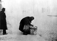 Image of an elderly woman bent over a trash can