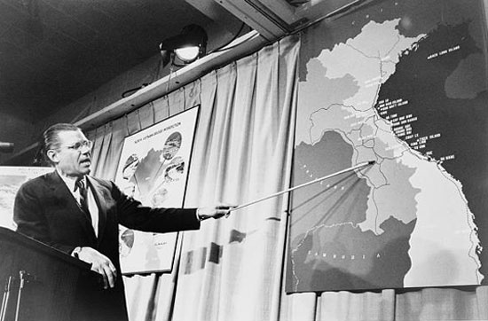 Image of Robert McNamara pointing to a map of Vietnam at press conference.