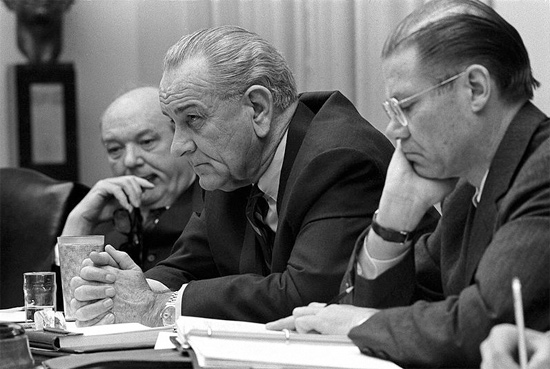 President Lyndon B. Johnson cabinet meeting with Secretary of State Dean Rusk, and Secretary of Defense Robert McNamara. All men are seated at a table with serious looks on their faces.