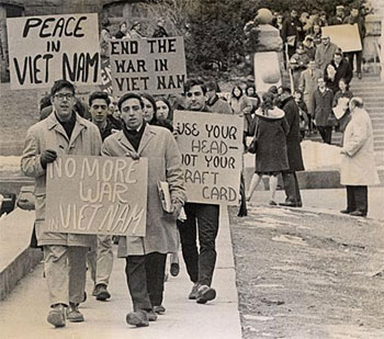 A photograph of Vietnam War protesters carrying signs that read 'Peace in Vietnam, No More War in Vietnam', and 'Use your head, not your draft-card'.