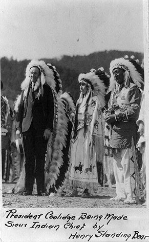 Image of Calvin Coolidge in Sioux Indian headdress, surrounded by a Sioux Indian Chief and woman.