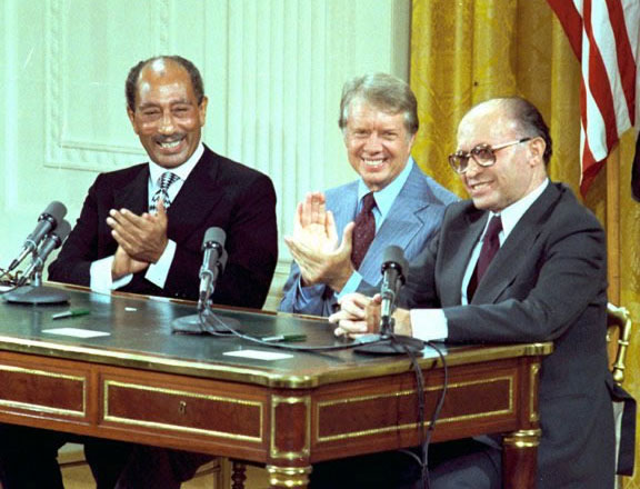 Image of Sadat, Carter, and Begin seated at a desk behind microphones