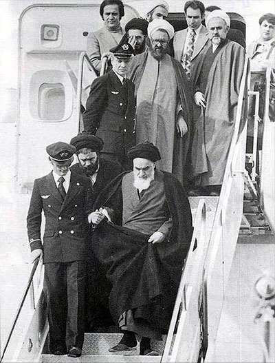 Image of Khomeini exiting an airplane, led by a pilot and surrounded by his followers