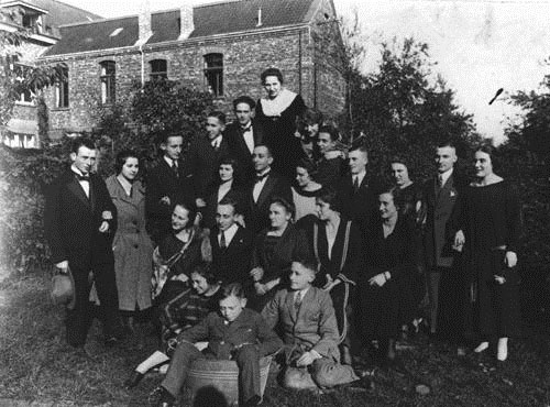 Photo of a German-Jewish family of several men, women, boys and girls who are gathered in the front yard of a two-story home.
